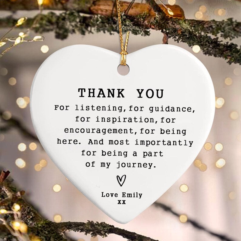 White heart-shaped ornament with gold hanging cord. The ornament has the words "THANK YOU" at the top, followed by a message of gratitude. A heart symbol and the words "Love Emily" are at the bottom.