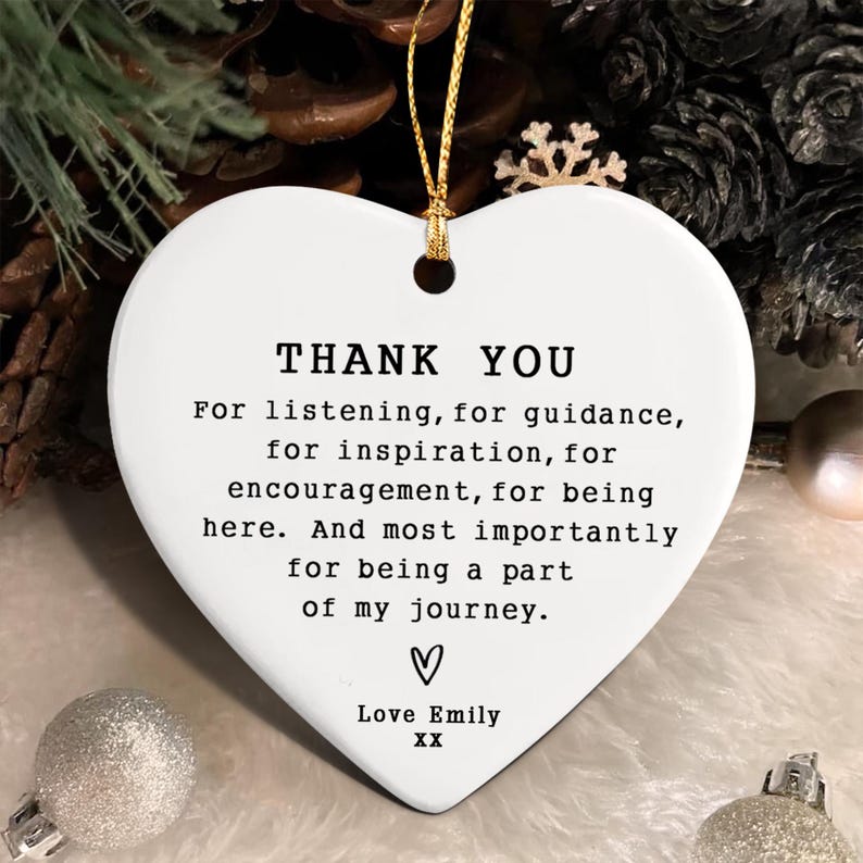White heart-shaped ornament with gold string for hanging. The ornament has the words "THANK YOU" and a message of gratitude printed in black. Includes a heart symbol and the name "Love Emily".