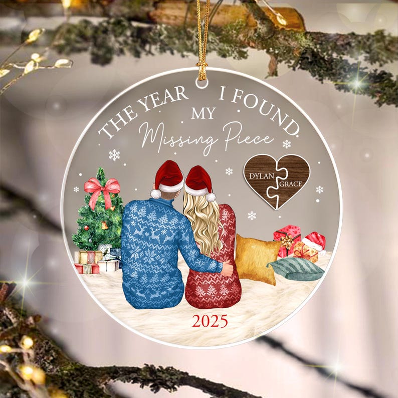 A round ceramic Christmas ornament featuring a couple wearing Santa hats and holiday sweaters, sitting together. The text reads THE YEAR I FOUND MY Missing Piece and 2025.