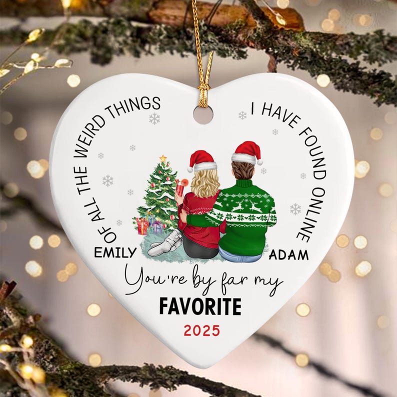 A heart-shaped white ceramic ornament featuring a Christmas tree and two figures wearing Santa hats. The text reads: OF ALL THE WEIRD THINGS I HAVE FOUND ONLINE YOU'RE BY FAR MY FAVORITE.