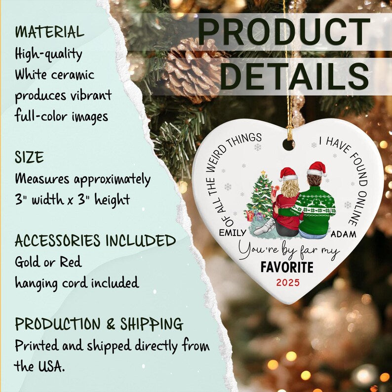 A white heart-shaped ceramic ornament featuring a printed illustration of two people in holiday sweaters and Santa hats sitting by a Christmas tree.