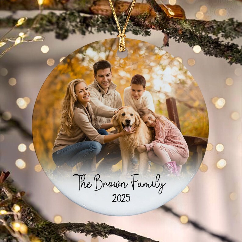 A round ceramic ornament featuring a photograph of a family with a golden retriever dog in an autumn setting. The text "The Brown Family" is printed in black script above the year "2025" in a simple black font at the bottom.