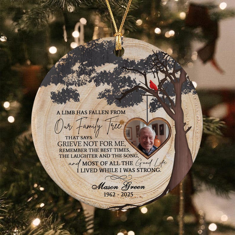 A round ceramic memorial ornament featuring a wood grain background, a tree silhouette with a red cardinal, and a heart-shaped photo frame. It includes the text A LIMB HAS FALLEN FROM Our Family Tree, Mason Green, and 1962-2025.