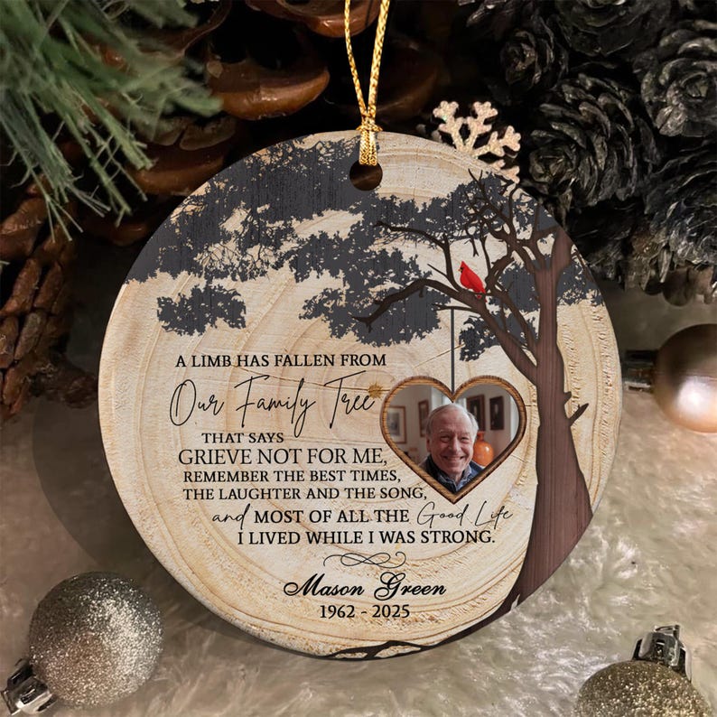 A round wooden memorial ornament featuring a tree silhouette with a red cardinal, a heart-shaped photo frame containing a portrait of a man, and the text A LIMB HAS FALLEN FROM Our Family Tree, Mason Green, 1962-2025.