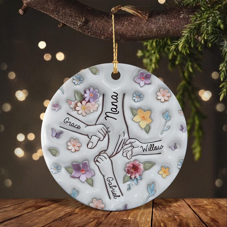 A round white ceramic ornament featuring a central illustration of four hands holding each other. The names Nana, Grace, Willow, and Gabriel are written on the arms.