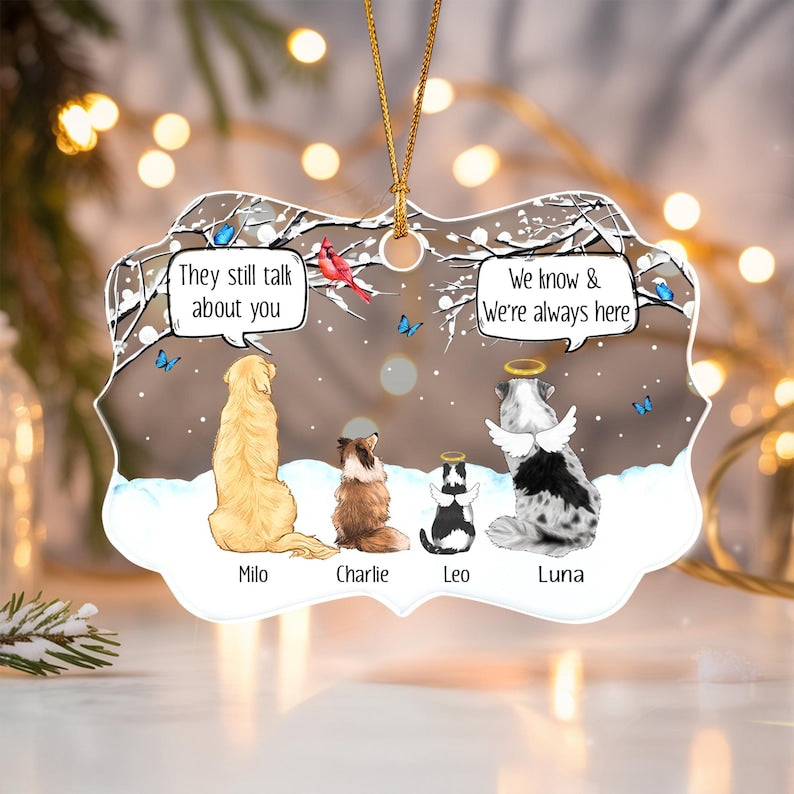 A decorative ornament featuring four pets sitting in snow under a winter tree. The pets are labeled Milo, Charlie, Leo, and Luna. Two speech bubbles contain the text: They still talk about you and We know & We're always here.