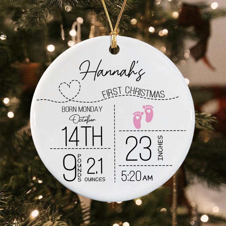 A round white ceramic ornament with a gold string featuring black text that reads Hannah's First Christmas, Born Monday October 14th, 9 pounds 2.1 ounces, 23 inches, and 5:20 AM.