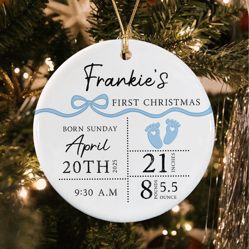 A round white ceramic ornament featuring a blue ribbon graphic and the text Frankie's FIRST CHRISTMAS.