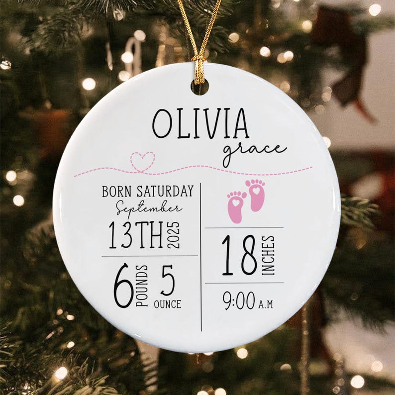 A round white ceramic ornament with a gold string featuring the name Olivia Grace, a pink heart-shaped dotted line, and pink baby footprints.