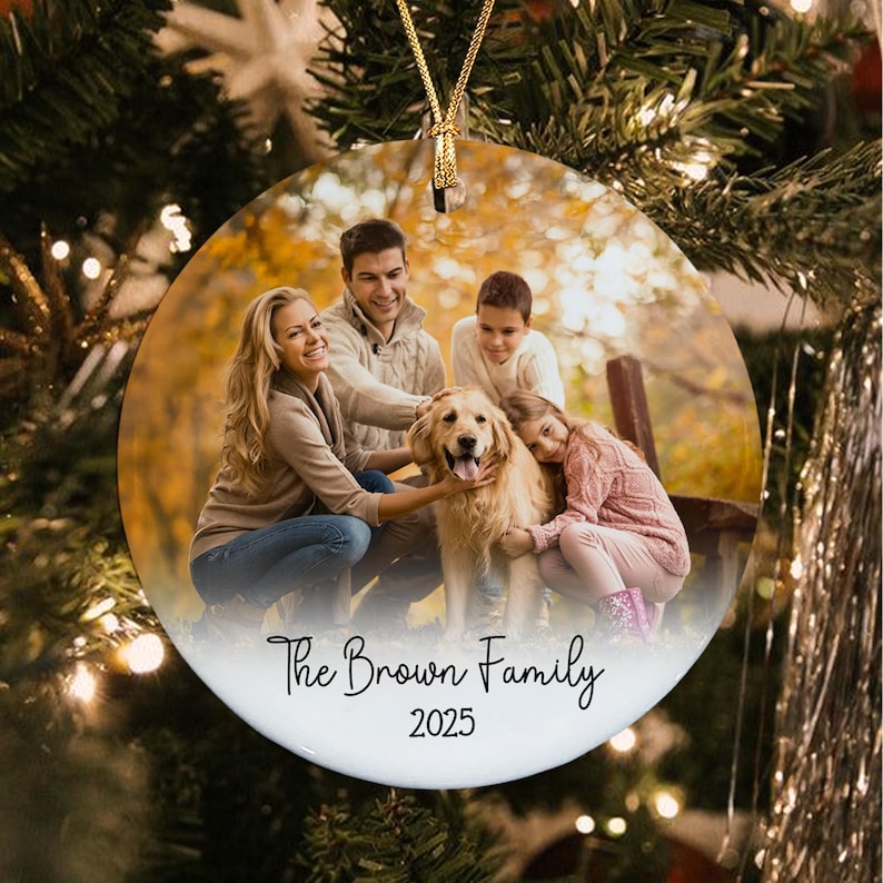 A round ceramic Christmas ornament featuring a printed photograph of a family of four with a golden retriever dog in an outdoor setting.