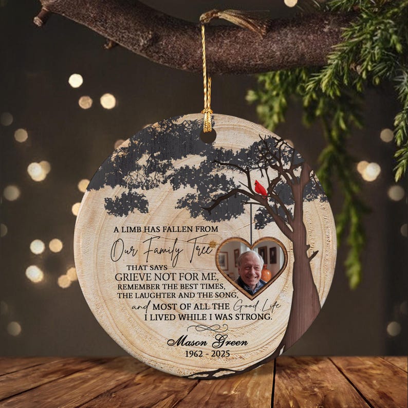 A round wooden memorial ornament featuring a printed tree silhouette, a red cardinal, and a heart-shaped photo frame. The text reads: A LIMB HAS FALLEN FROM Our Family Tree THAT SAYS GRIEVE NOT FOR ME, MASON GREEN 1962-2025.