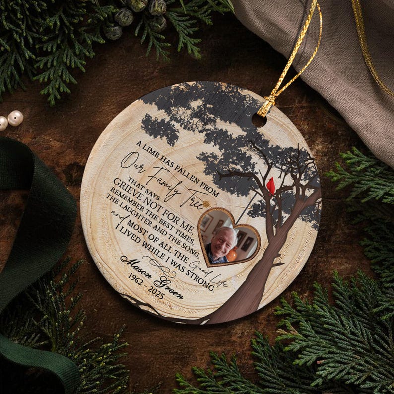 A round wooden memorial ornament featuring a printed tree silhouette with a red cardinal, a heart-shaped photo frame, and the text A LIMB HAS FALLEN FROM OUR FAMILY TREE, GRIEVE NOT FOR ME, MASON GREEN 1962-2025.