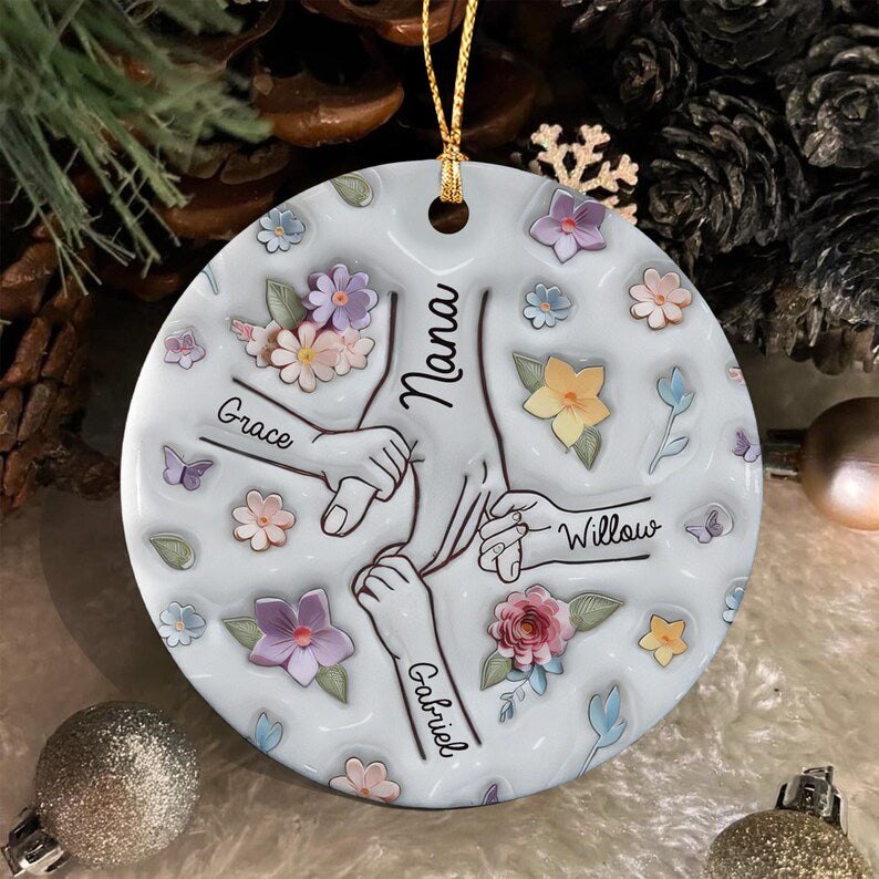A round white ceramic ornament featuring a central illustration of three hands holding onto a central point. The names Grace, Willow, and Gabriel are written on the arms, with Nana in the center.