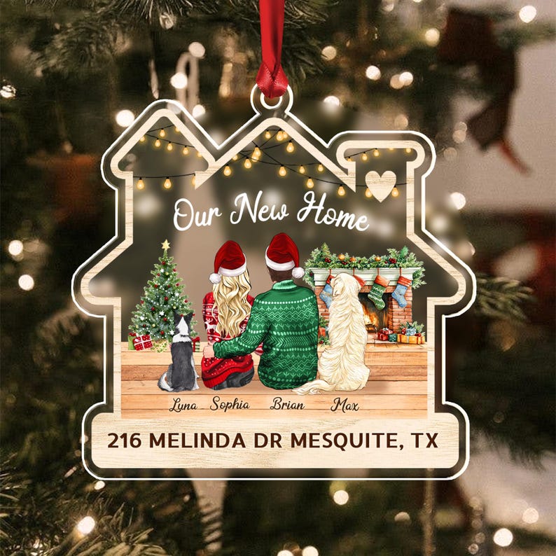 A house-shaped Christmas ornament featuring a couple and two dogs sitting before a fireplace and tree. The text reads Our New Home, the names Luna, Sophia, Brian, Max, and the address 216 MELINDA DR MESQUITE, TX.