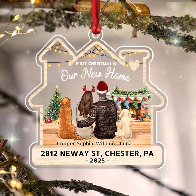 A house-shaped Christmas ornament featuring a red ribbon, displaying the text FIRST CHRISTMAS IN Our New Home.