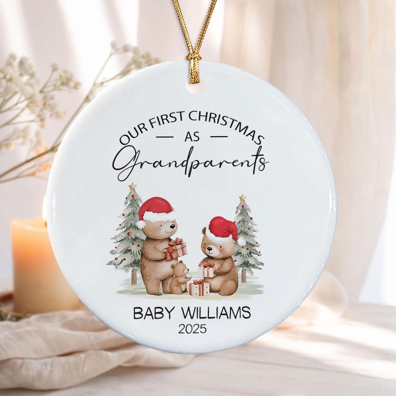 A round white ceramic ornament hanging from a gold string. It features the text "OUR FIRST CHRISTMAS AS Grandparents" above an illustration of three brown bears in Santa hats with gifts and two Christmas trees.