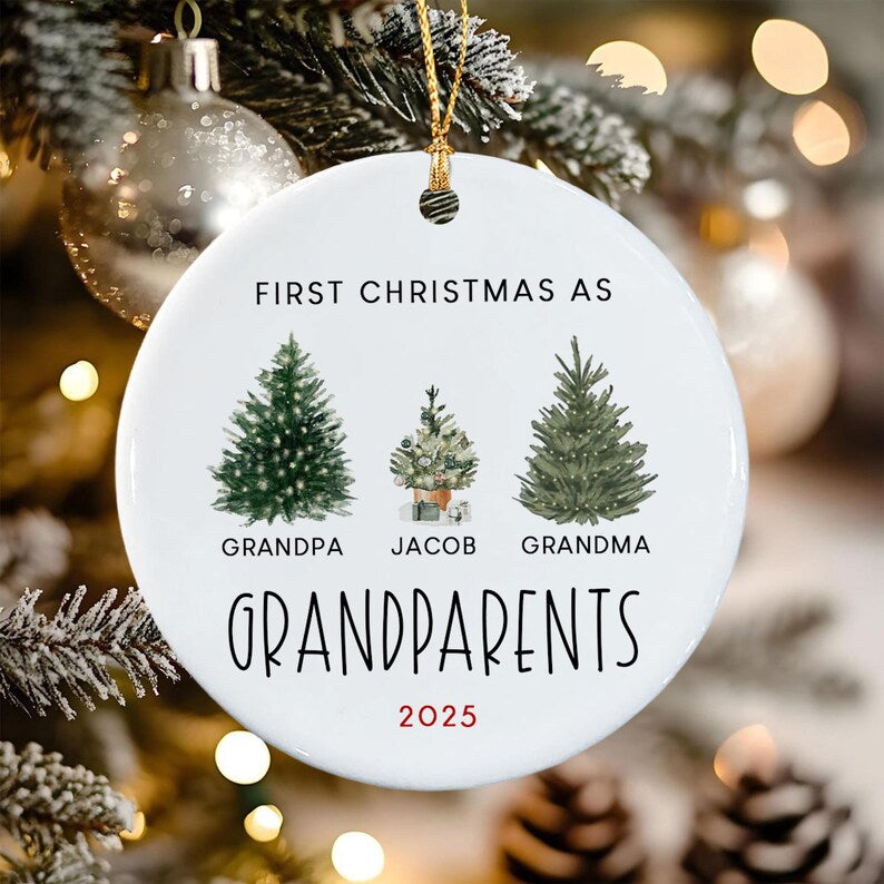 A round white ceramic Christmas ornament featuring the text FIRST CHRISTMAS AS GRANDPARENTS and 2025. It displays three illustrated evergreen trees with the names GRANDPA, JACOB, and GRANDMA printed below each respective tree.