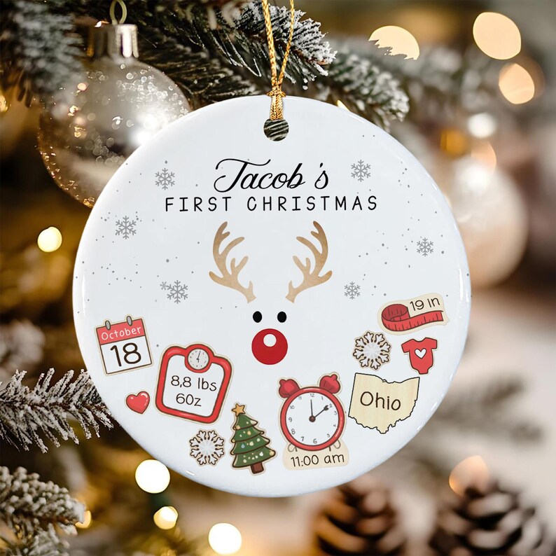 A round white ceramic ornament featuring the text 'Jacob's FIRST CHRISTMAS' and a reindeer graphic.