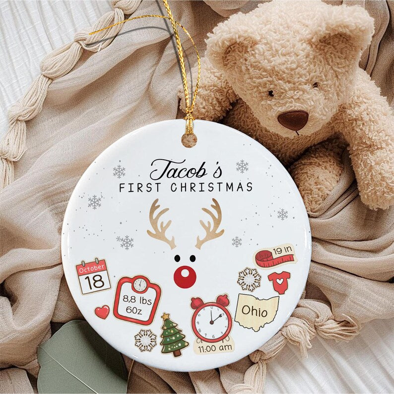 A round white ceramic Christmas ornament featuring the text 'Jacob's FIRST CHRISTMAS' and a reindeer graphic.