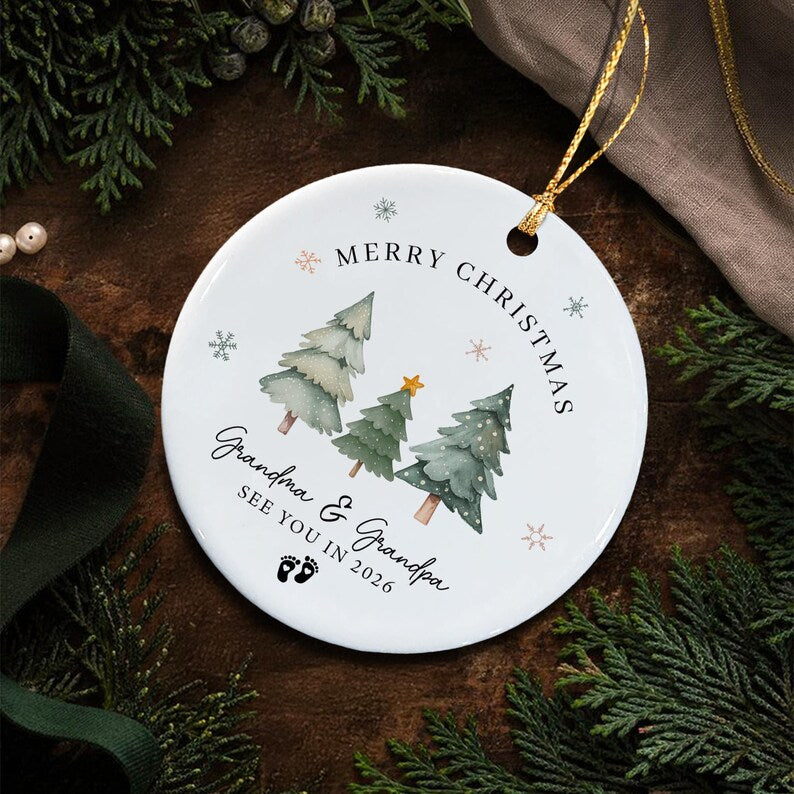 A round white ceramic Christmas ornament featuring three watercolor-style green pine trees, a small yellow star, and snowflakes.