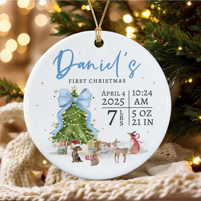 A round white ceramic ornament with a gold string featuring the text Daniel's FIRST CHRISTMAS, the date April 4 2025, time 10:24 AM, and birth stats 7 LBS 5 OZ 21 IN.