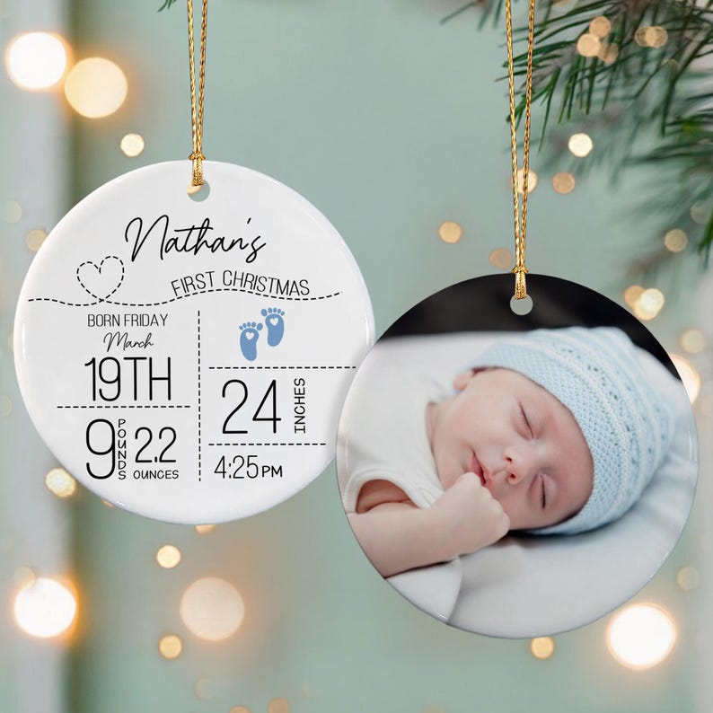 Two round white ceramic ornaments with gold hanging strings. One ornament features black text reading Nathan's First Christmas, birth details including 19th March, 9 pounds 2.2 ounces, 24 inches, and 4:25 PM.