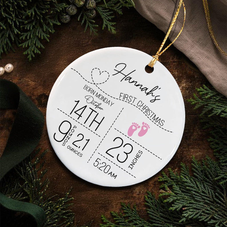 A round white ceramic ornament featuring black text that reads Hannah's First Christmas, Born Monday October 14th, 9 pounds 21 ounces, 23 inches, and 5:20 AM.