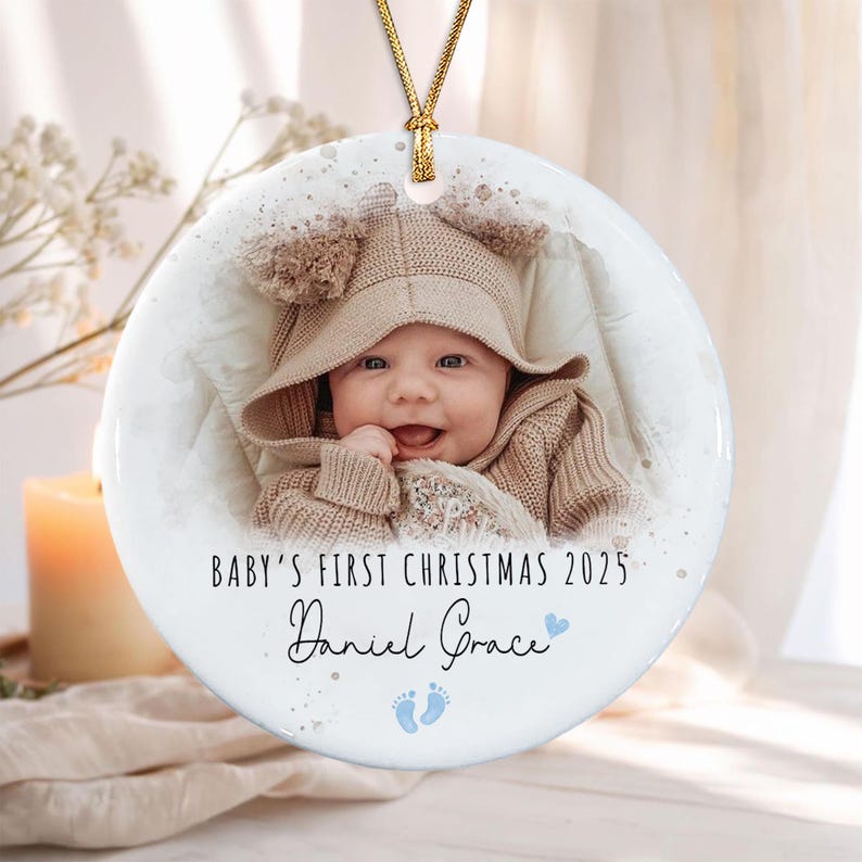 A round white ceramic ornament featuring a photograph of a baby wearing a tan knit hood.