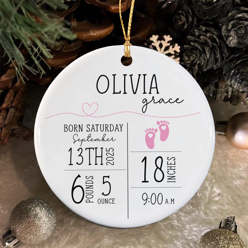 A round white ceramic ornament featuring the name Olivia Grace, a pink dashed line with a heart, and birth details including Saturday, September 13th 2025, 6 pounds 5 ounces, 18 inches, and 9:00 A.M. with two pink baby footprints.