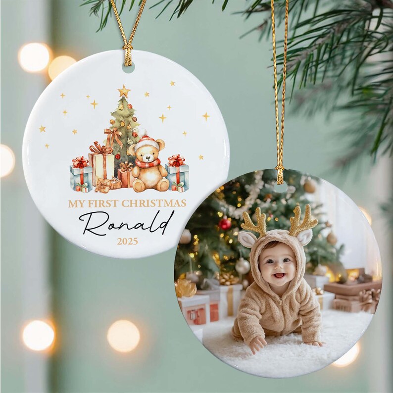 Two round ceramic ornaments with gold hanging strings. One features a watercolor illustration of a teddy bear, Christmas tree, and gifts with the text MY FIRST CHRISTMAS Ronald 2025.