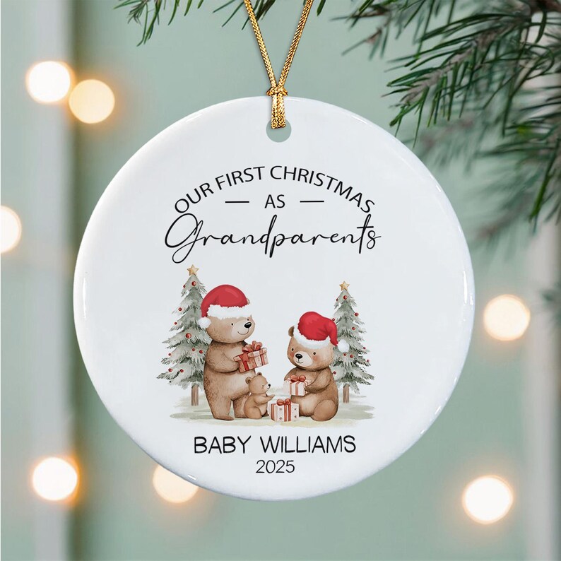 A round white ceramic Christmas ornament hanging by a gold string. It features a watercolor illustration of three brown bears wearing red Santa hats, holding gifts, with two pine trees.