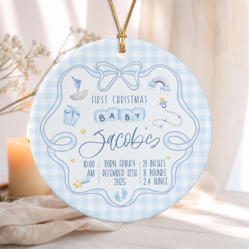 A round ceramic ornament with a light blue gingham pattern, featuring a central bow graphic, a sailboat, a pacifier, and baby blocks spelling BABY.