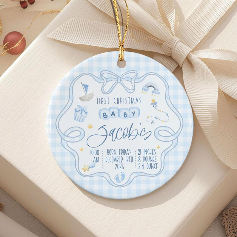 A round ceramic ornament with a light blue gingham pattern, featuring a gold hanging string. The design includes a sailboat, rainbow, pacifier, and stars.