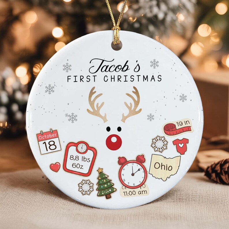 A round white ceramic ornament with a gold string, featuring the text 'Jacob's FIRST CHRISTMAS'.