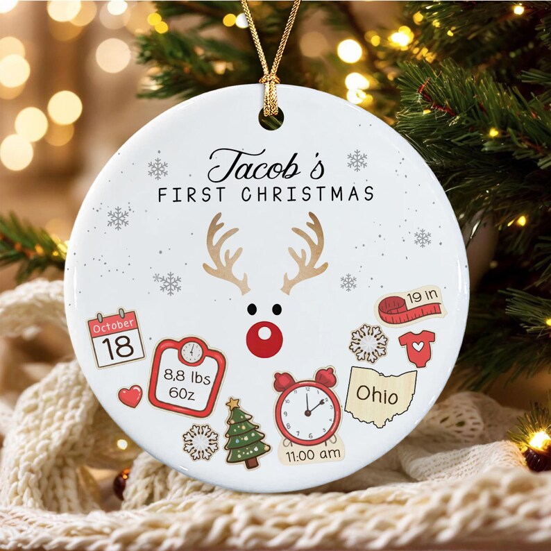 A round white ceramic Christmas ornament featuring the text 'Jacob's FIRST CHRISTMAS' and a reindeer graphic.
