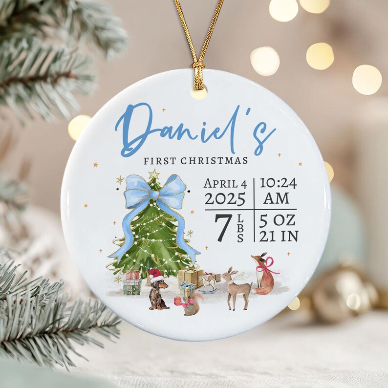 A round white ceramic ornament with a gold string featuring the text Daniel's First Christmas, birth date April 4 2025, time 10:24 AM, and weight 7 lbs 5 oz, 21 in.