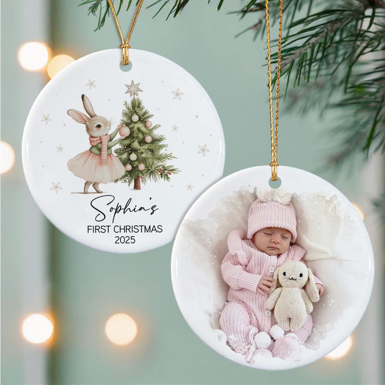 Two round white ceramic ornaments with gold hanging strings. One features a watercolor rabbit in a tutu decorating a Christmas tree with the text Sophia's FIRST CHRISTMAS 2025.