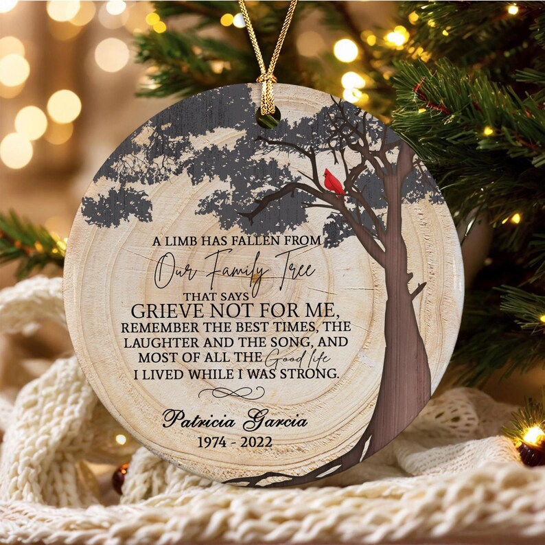 A round, wood-slice style ornament featuring a printed tree silhouette with a red cardinal. Text reads: A LIMB HAS FALLEN FROM Our Family Tree THAT SAYS GRIEVE NOT FOR ME, REMEMBER THE BEST TIMES, Patricia Garcia 1974-2022.