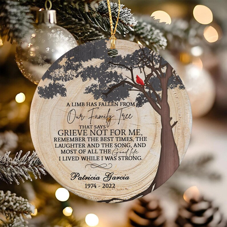 A round ceramic ornament with a wood grain texture print featuring a dark tree silhouette and a red cardinal. The text reads: A LIMB HAS FALLEN FROM OUR FAMILY TREE THAT SAYS GRIEVE NOT FOR ME, Patricia Garcia 1974-2022.
