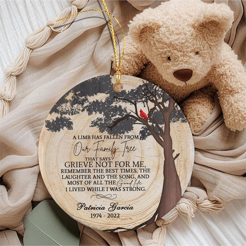 A round wooden ornament featuring a tree graphic with a red cardinal, inscribed with the text: A LIMB HAS FALLEN FROM OUR FAMILY TREE THAT SAYS GRIEVE NOT FOR ME, REMEMBER THE BEST TIMES, THE LAUGHTER AND THE SONG.