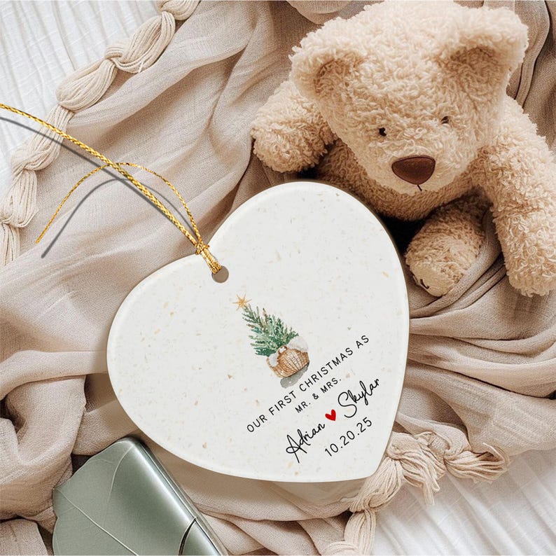 A heart-shaped white ceramic ornament featuring a watercolor illustration of a Christmas tree in a basket, with the text "OUR FIRST CHRISTMAS AS MR. & MRS.
