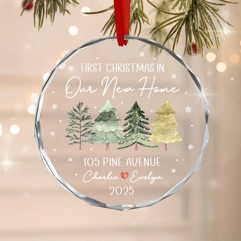 A circular clear glass Christmas ornament with a faceted edge, featuring the text First Christmas in Our New Home, 105 Pine Avenue, Charlie, Evelyn, and 2025.