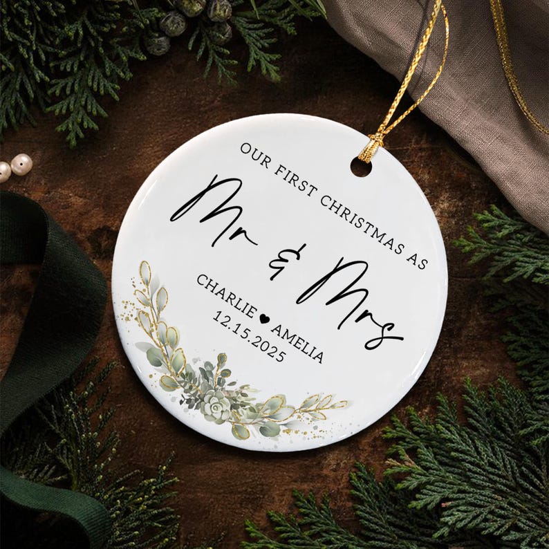 A round white ceramic ornament featuring the black text "OUR FIRST CHRISTMAS AS Mr & Mrs" with the names "CHARLIE" and "AMELIA" separated by a heart and the date "12.15.2025".