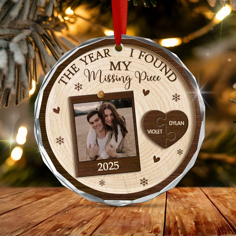 A round, faceted glass ornament with a wood-grain background. It features the text "THE YEAR I FOUND MY Missing Piece" and "2025" on a photo frame graphic.