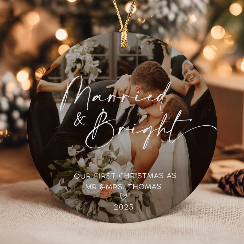 A round ceramic ornament featuring a photograph of a couple kissing at their wedding. The text reads Married & Bright, OUR FIRST CHRISTMAS AS MR. & MRS. THOMAS, and 2025. A gold string is attached to the top for hanging.