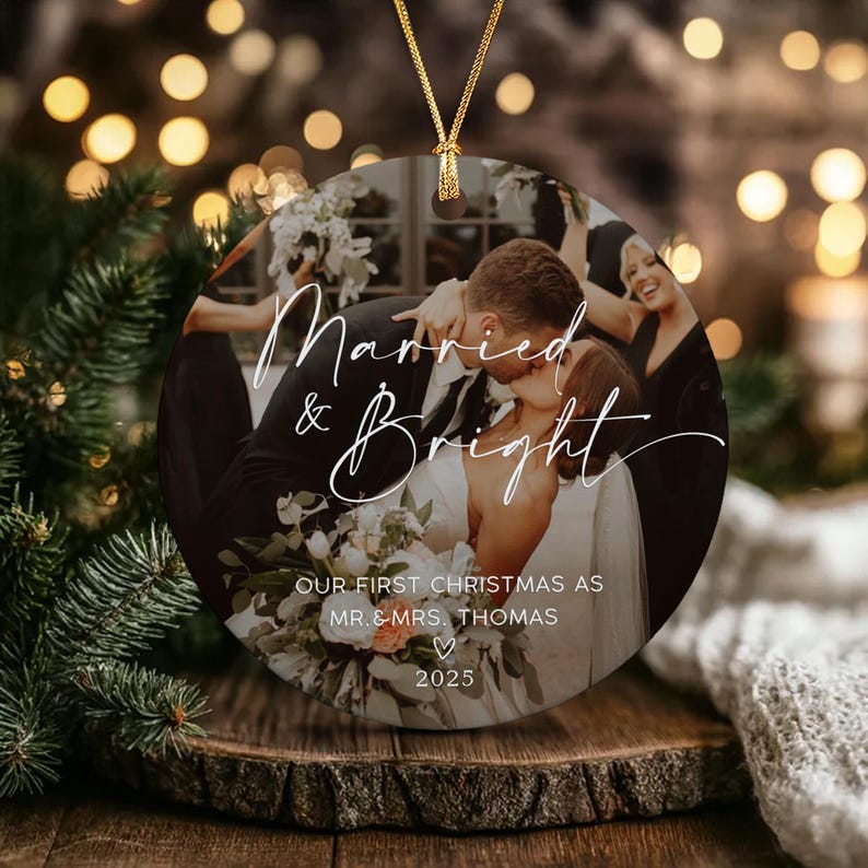 A round ceramic ornament featuring a photograph of a couple kissing, with white cursive text reading Married & Bright, followed by the text OUR FIRST CHRISTMAS AS MR. & MRS. THOMAS, a heart icon, and the year 2025.