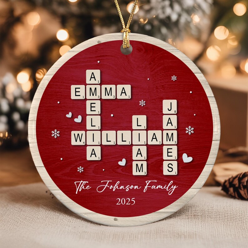 A round, red, wood-grain patterned Christmas ornament featuring a crossword-style arrangement of letter tiles spelling the names Emma, Amelia, William, Liam, and James. The text The Johnson Family and 2025 are printed below.