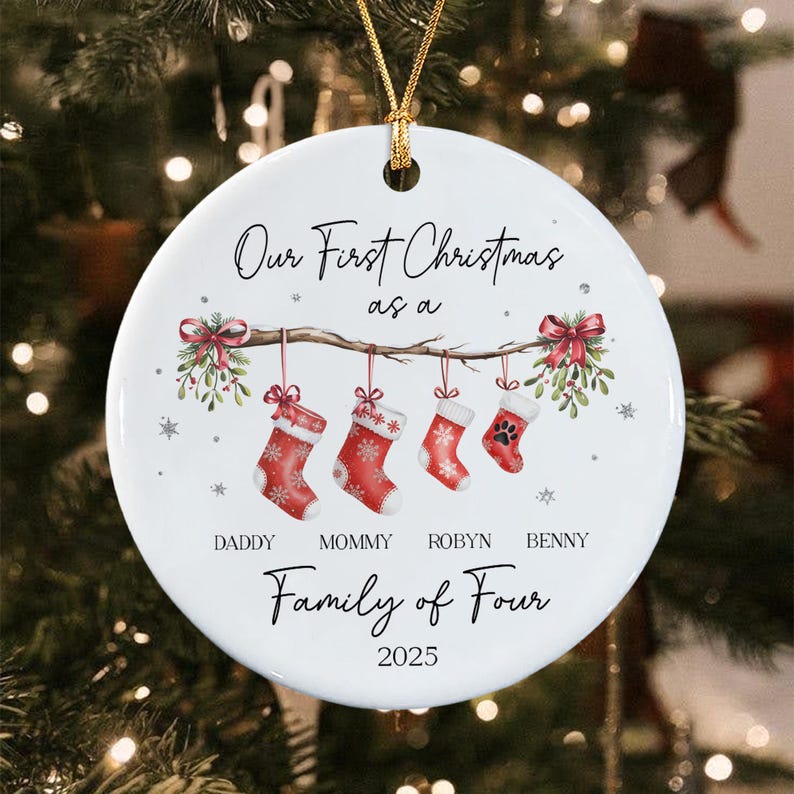 A round white ceramic Christmas ornament featuring the text Our First Christmas as a Family of Four 2025. The design includes a branch with four hanging red stockings, mistletoe, and the names Daddy, Mommy, Robyn, and Benny.