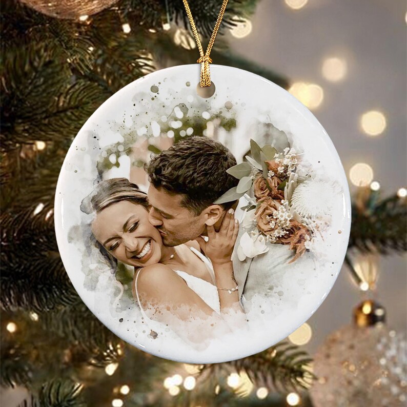 A round white ceramic ornament featuring a watercolor-style printed image of a couple embracing. The person on the left smiles while the person on the right kisses their cheek.