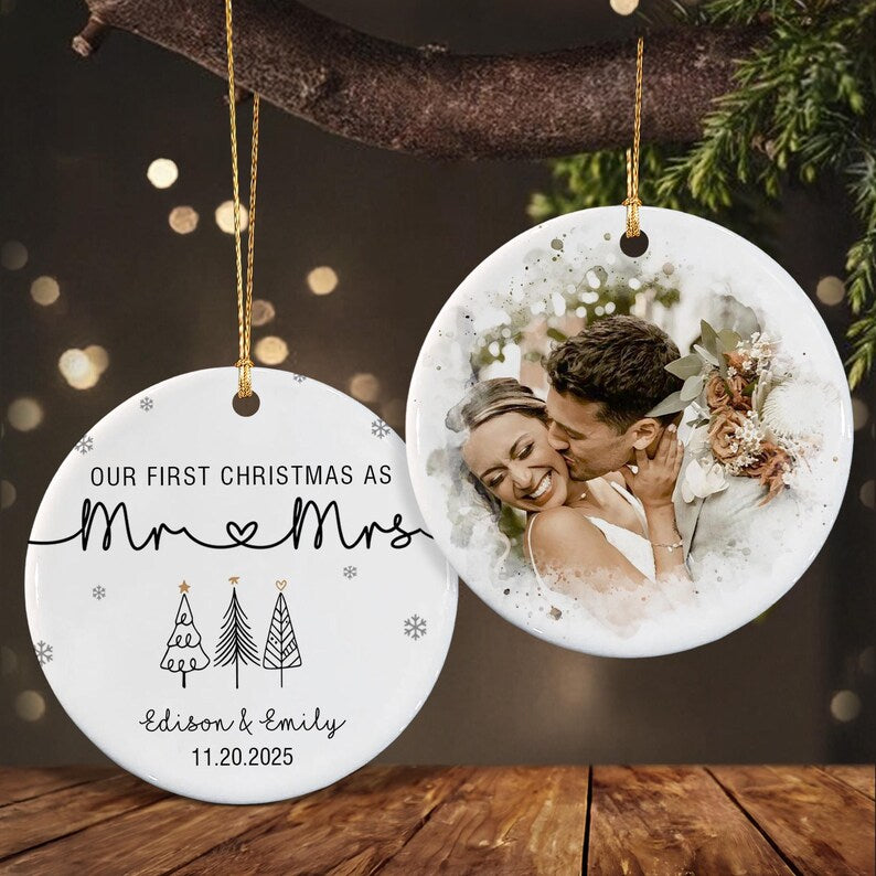 Two round white ceramic ornaments hanging by gold strings. One features the black text "OUR FIRST CHRISTMAS AS Mr & Mrs", three line-art Christmas trees, and the names "Edison & Emily" with the date "11.20.2025".